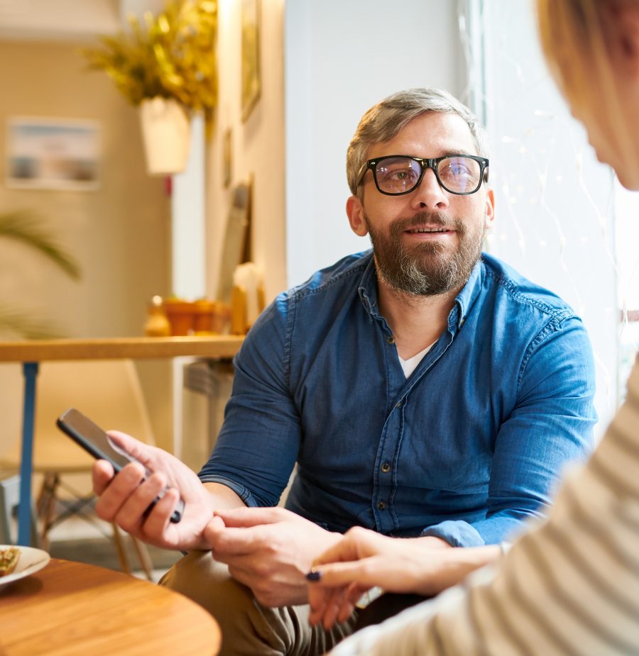 Casual man in eyeglasses looking at his girlfriend during conversation in cozy cafe